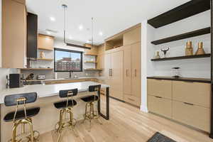 Kitchen with open shelves, light wood finish cabinetry, a peninsula, and a breakfast bar area