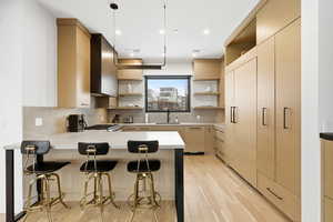 Kitchen featuring open shelves, a breakfast bar, light wood finish cabinetry, a peninsula, and modern cabinets