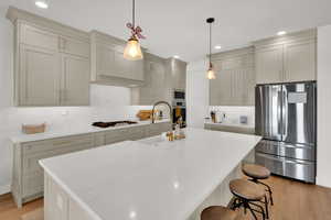Kitchen with stainless steel appliances, light wood-type flooring, a breakfast bar area, and hanging light fixtures
