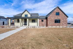 Modern inspired farmhouse featuring covered porch, a front yard, board and batten siding, brick siding, and roof with shingles