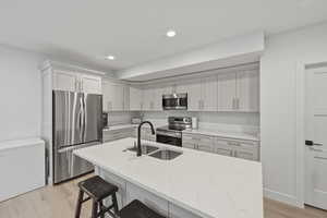 Kitchen with stainless steel appliances, white cabinetry, light stone counters, light wood finished floors, and an island with sink
