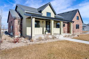 Modern farmhouse style home featuring board and batten siding, covered porch, a front yard, brick siding, and a shingled roof