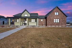 Modern farmhouse with a porch, a lawn, board and batten siding, and brick siding