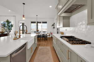 Kitchen featuring stainless steel appliances, light stone counters, light wood-type flooring, a kitchen island with sink, and suspended lighting