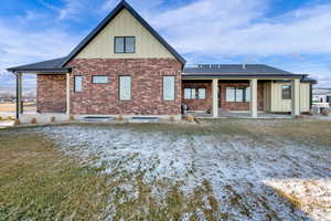 Snow covered back of property featuring board and batten siding, a patio area, brick siding, and a yard