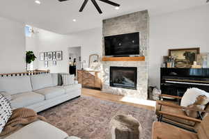 Living room featuring wood finished floors, a stone fireplace, ceiling fan, and recessed lighting