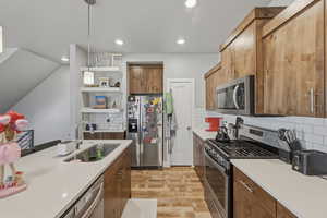 Kitchen with stainless steel appliances, wood finish cabinetry, light wood-style flooring, decorative backsplash, and light stone counters