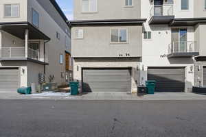 Rear view of house featuring stucco siding, a balcony, a garage, and stone siding
