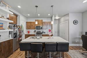 Kitchen with stainless steel appliances, decorative backsplash, open shelves, and an island with sink