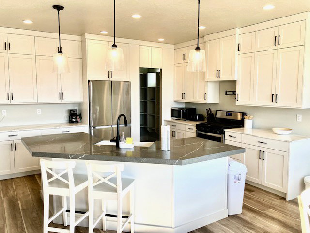 Kitchen featuring stainless steel appliances, white cabinets, light wood-style floors, decorative light fixtures, and a breakfast bar area