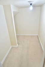 Under stairway area with light carpet and a textured ceiling