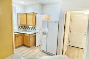Kitchen featuring light countertops, white refrigerator with ice dispenser, light wood-type flooring, tasteful backsplash, and light wood finish cabinets