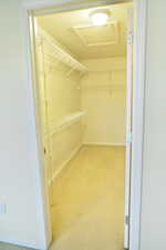 Walk in closet featuring attic access and light carpet