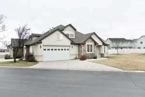 View of front facade with stone siding, driveway, roof with shingles, a garage, and stucco siding