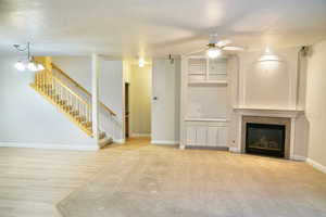 Unfurnished living room featuring a tile fireplace, ceiling fan, and a chandelier
