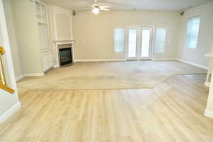 Unfurnished living room with a fireplace with flush hearth, french doors, built in features, a ceiling fan, and light wood finished floors