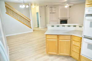 Kitchen with double oven, light countertops, light wood finish cabinets, suspended lighting, and open floor plan
