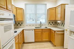 Kitchen featuring white appliances, light countertops, light wood-style flooring, and tasteful backsplash