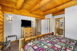 Bedroom featuring a wooden ceiling with exposed beams, light colored carpet, and ensuite bath
