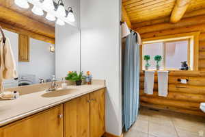 Bathroom with log walls, a wood ceiling with exposed beams, a shower with curtain, vanity, and washer / clothes dryer
