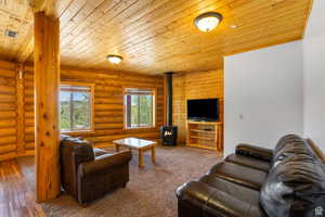 Carpeted living area featuring a wood stove, wood ceiling, and rustic walls
