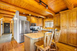 Kitchen featuring rustic walls, track lighting, stainless steel appliances, light stone countertops, and a breakfast bar