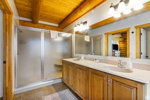 Bathroom featuring double vanity, a wooden ceiling with exposed beams, a shower stall, and dark tile patterned floors