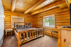 Bedroom with carpet flooring, rustic walls, and a wooden ceiling with exposed beams