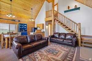 Carpeted living room with a vaulted wooden ceiling, rustic walls, and hanging lights