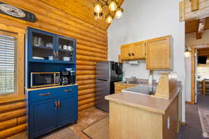 Kitchen with log walls, stainless steel appliances, a chandelier, light wood finish cabinetry, and a peninsula