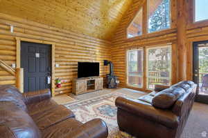 Carpeted living area with log walls, a vaulted wood ceiling, and a wood stove