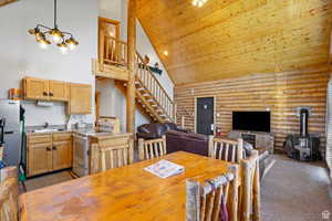Dining area with log walls, dark carpet, a wood stove, a vaulted wooden ceiling, and suspended lighting