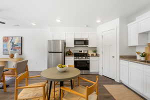 Kitchen featuring stainless steel appliances, dark stone counters, white cabinetry, dark wood-style flooring, and recessed lighting