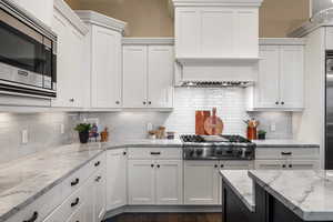 Two tone kitchen with stainless steel appliances, light stone countertops, two tone cabinetry, decorative backsplash, and dark wood-type flooring