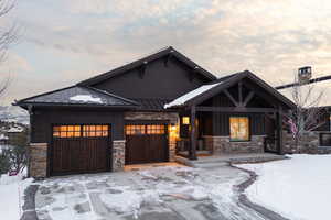 View of front facade featuring a standing seam roof, a porch, stone siding, and an attached garage