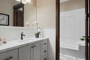 Bathroom with vanity, a bathtub, tile walls, and wainscoting