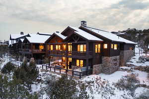 Snow covered back of property featuring stone siding, board and batten siding, a wooden deck, and a chimney