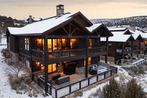 Snow covered house featuring board and batten siding, stone siding, a chimney, and outdoor furniture