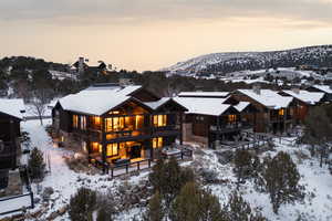 Snow covered house with a chimney, stone siding, and a deck with mountain view