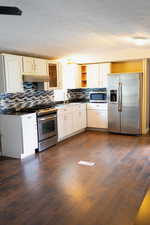 Kitchen featuring stainless steel appliances, open shelves, dark wood finished floors, white cabinets, and backsplash