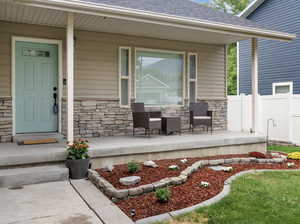 View of exterior entry with stone siding, a shingled roof, and a porch