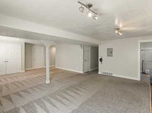 Finished below grade area featuring carpet flooring, a textured ceiling, and electric panel