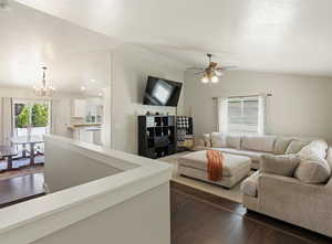 Living area featuring vaulted ceiling, a chandelier, a ceiling fan, and dark wood-style floors
