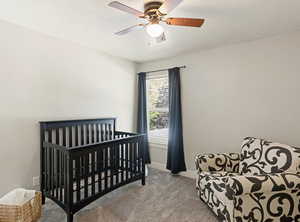 Bedroom with a nursery area, carpet flooring, a ceiling fan, and a textured ceiling