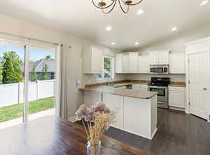 Kitchen with stainless steel appliances, white cabinetry, a peninsula, dark wood-type flooring, and suspended lighting