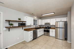 Kitchen with open shelves, stainless steel appliances, white cabinetry, a textured ceiling, and light tile patterned flooring