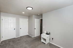 Unfurnished bedroom with dark colored carpet, a textured ceiling, and a closet