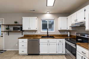 Kitchen featuring stainless steel appliances, white cabinets, open shelves, light tile patterned floors, and wooden counters