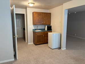 Kitchen with light carpet, a textured ceiling, wood finish cabinets, white fridge, and dark countertops