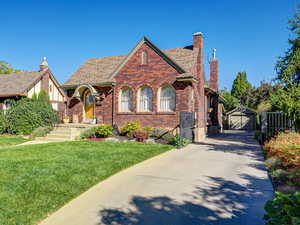 Tudor-style house with an outbuilding, brick siding, a detached garage, a chimney, and a front lawn